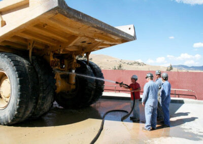 Group of men in blue suits using the in-ground wash system pad construction wash to wash a large construction vehicle