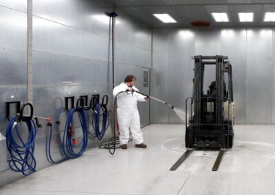 Person washing forklift in booth wash system