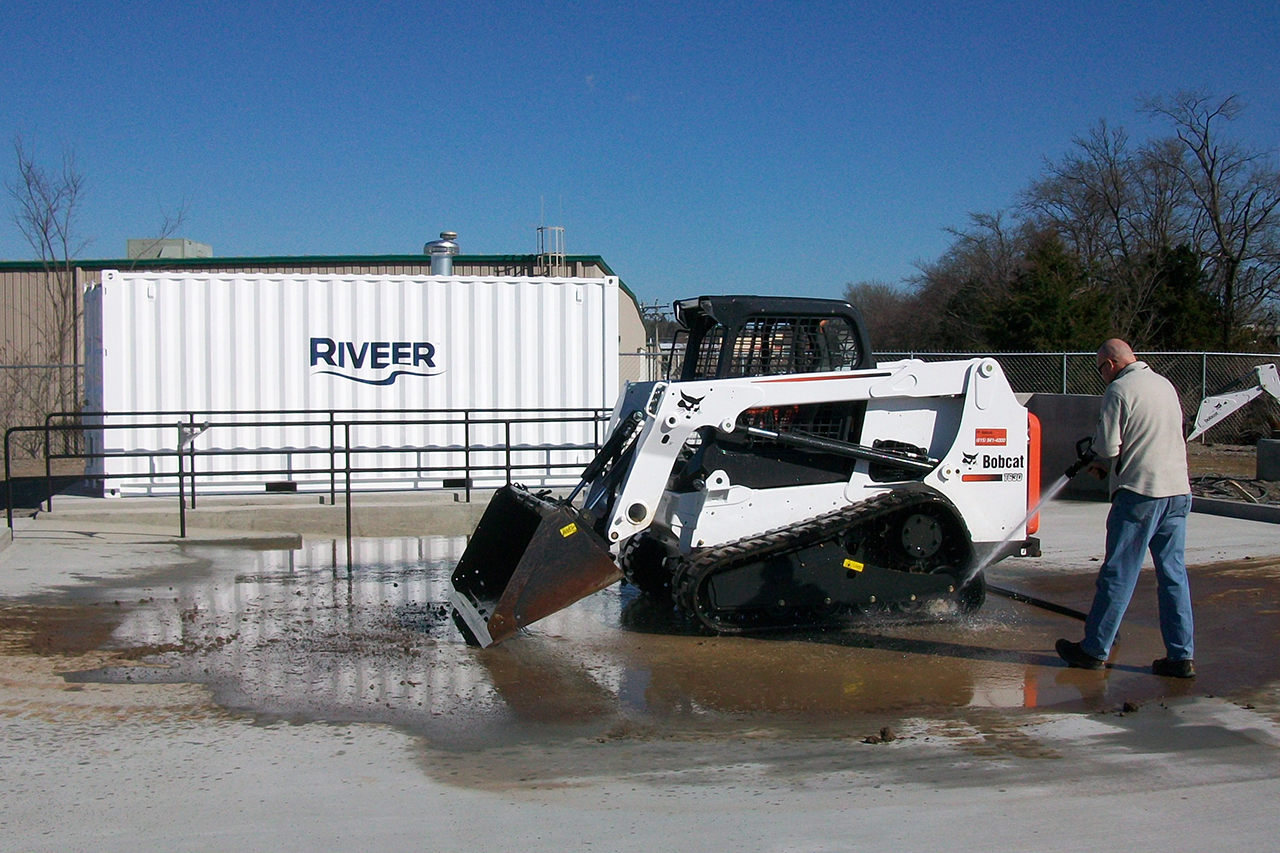 Man washing equipment with manual spray wand on concrete wash pad with Riveer container system.