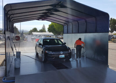 Person Washing a Sedan in a Covered Above Ground Vehicle Wash Booth with a Manual Spray Wand