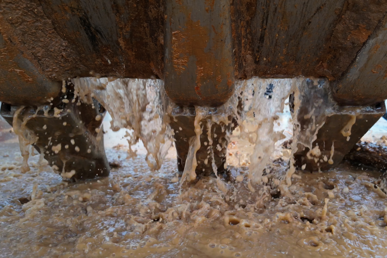 Muddy water running off the claws of an excavator bucket into a mud puddle