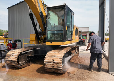 Person removing heavy much from large rental equipment with high pressure manual spray wand