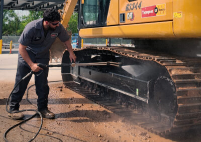 Person removing heavy mud from rental equipment with a high pressure manual spray wand