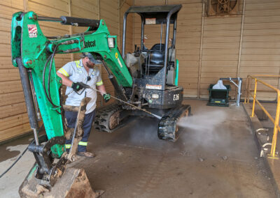 Person washing rental equipment with high pressure manual spray wand